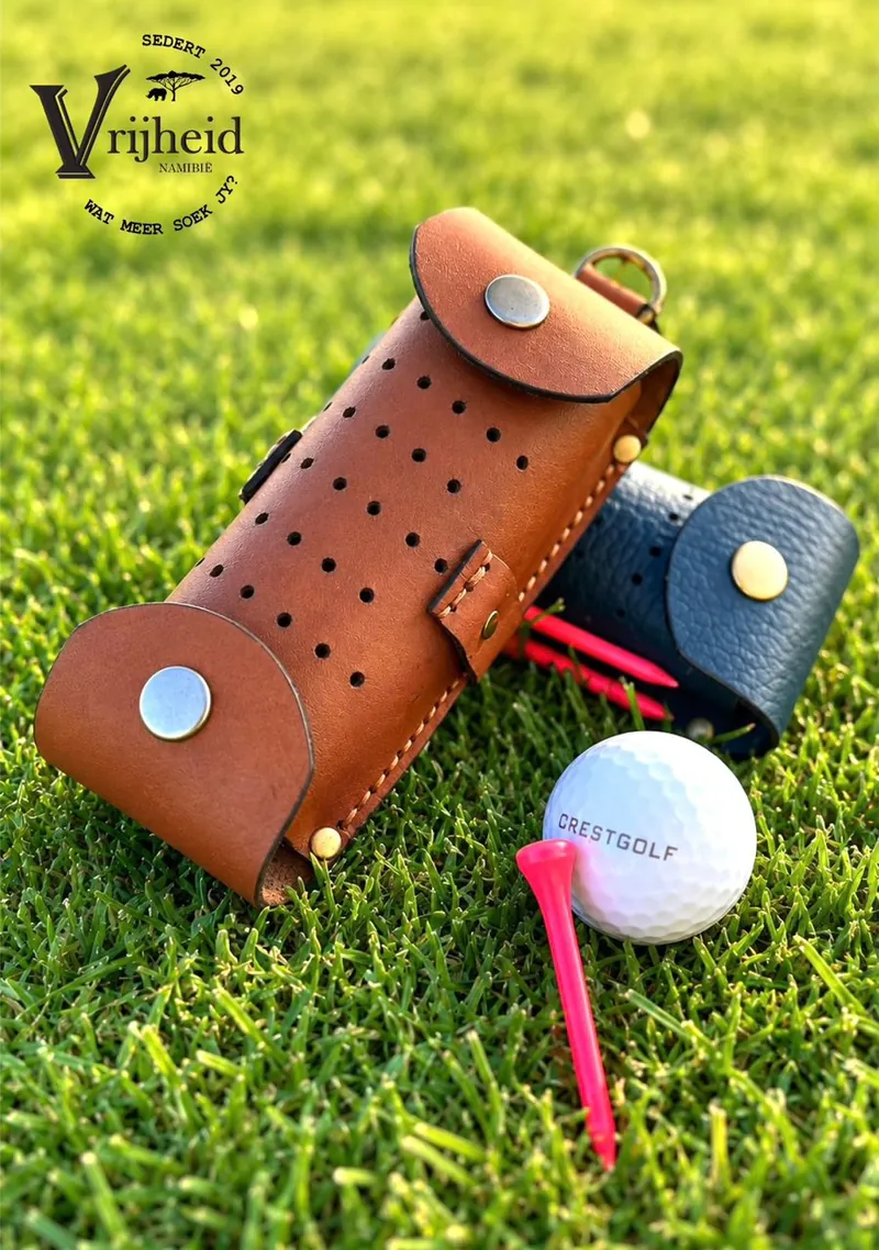 Tan leather golf ball case on the grass beside a golf ball and tee