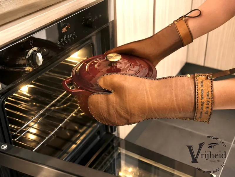 Engraved leather mitten lifting a cast-iron pot from the oven