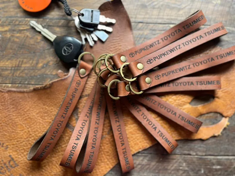 A batch of leather keychains engraved with a company name, with car keys on a leather hide